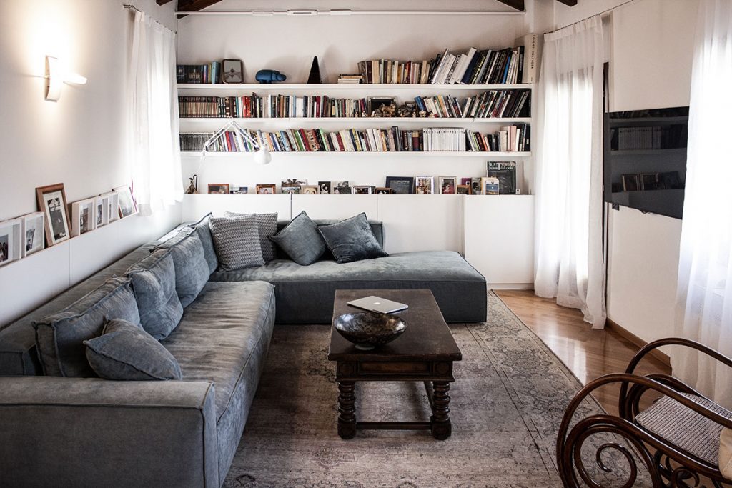 Foto dell'intero soggiorno con la libreria bianca, il divano sui toni del blu e il tavolino in lengo